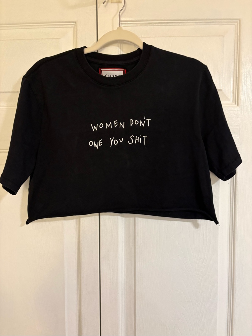 CHNGE Black Cropped Tee with White Statement Text. ‘Women Don’t Owe You Shit”